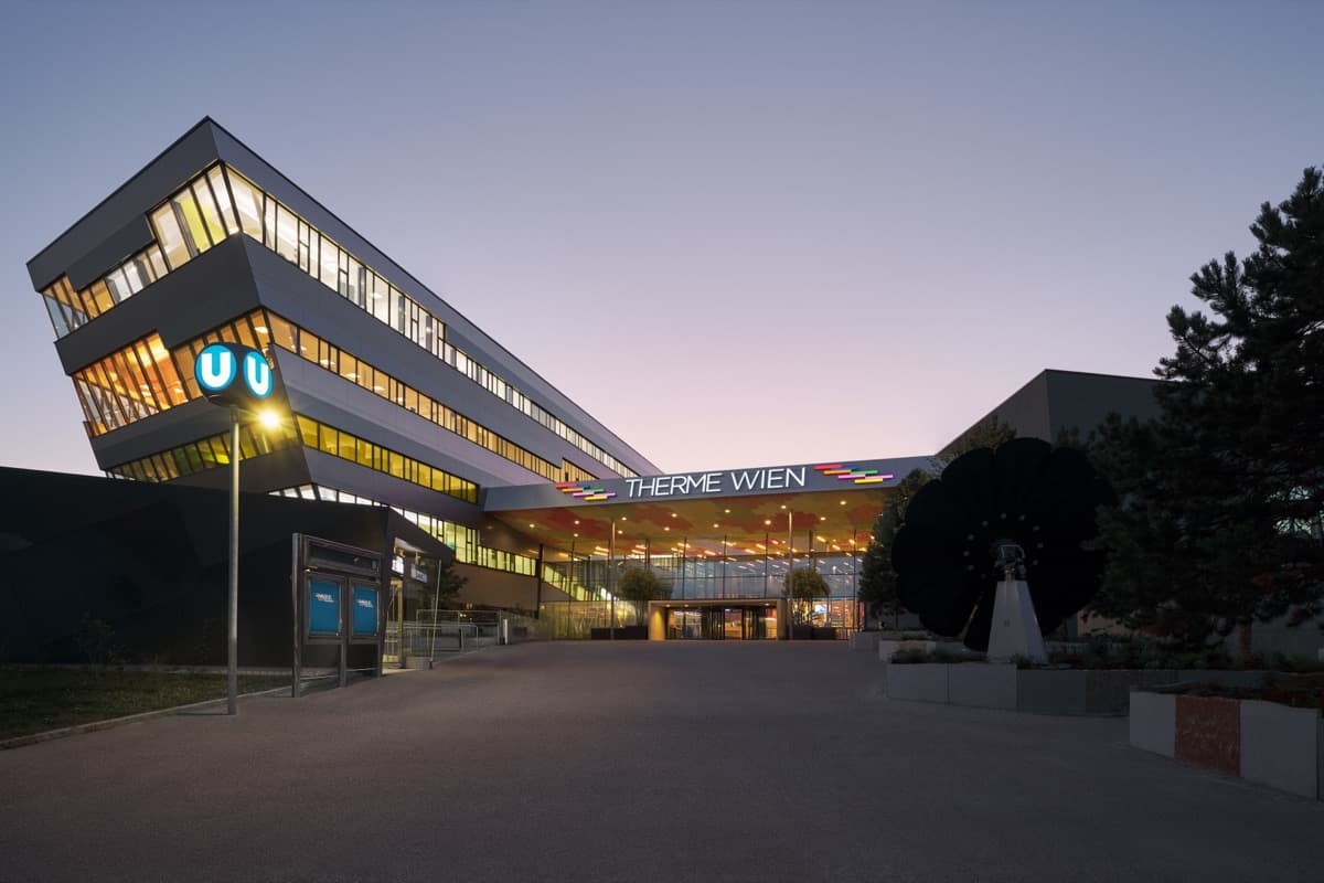 Beleuchtete Glasfassade der Therme Wien vor einem violetten Abendhimmel